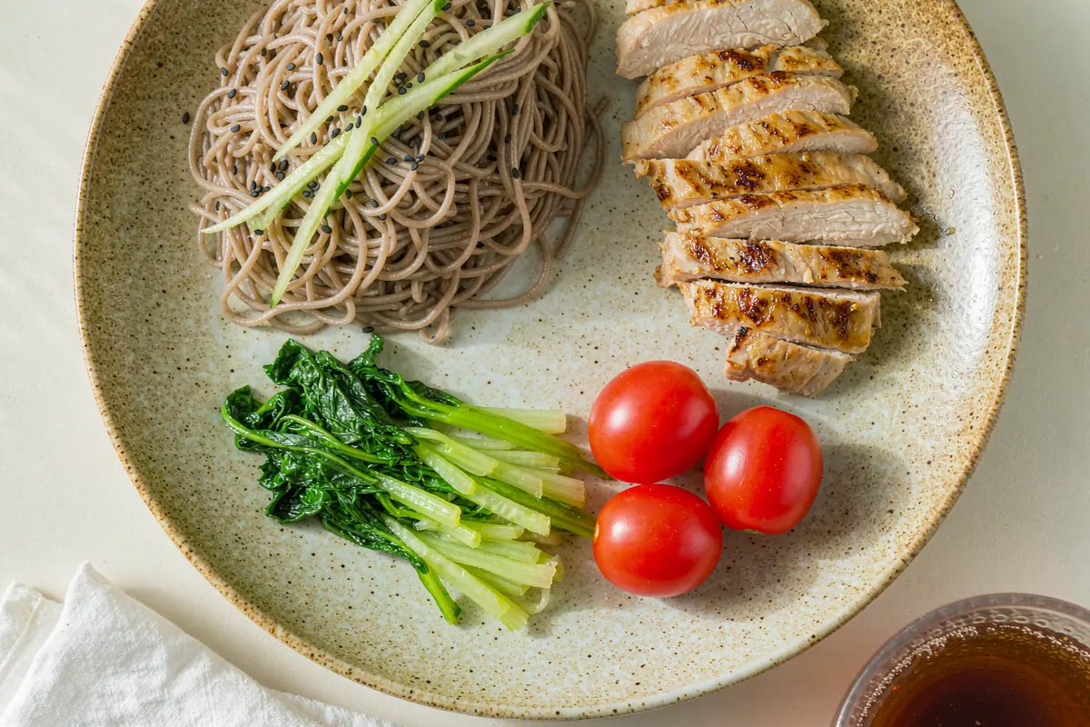 A light low-calorie lunch plate with chilled soba noodles, cucumber ribbons, grilled chicken, steamed greens and cherry tomatoes