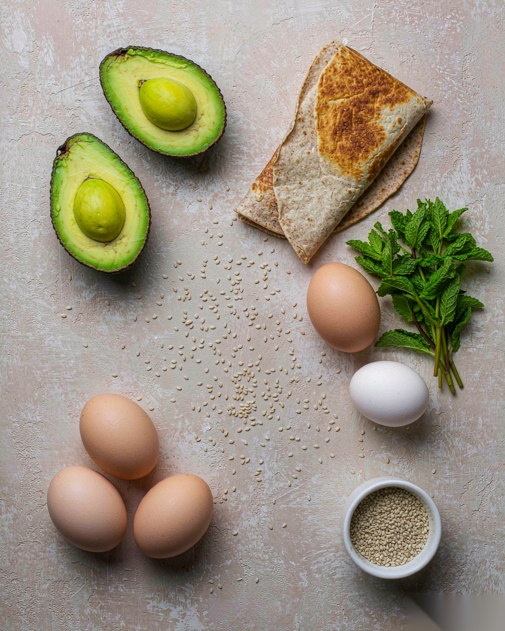 Flat lay of fresh ingredients for avocado egg roll — avocado, egg, whole wheat tortilla, sesame, herbs