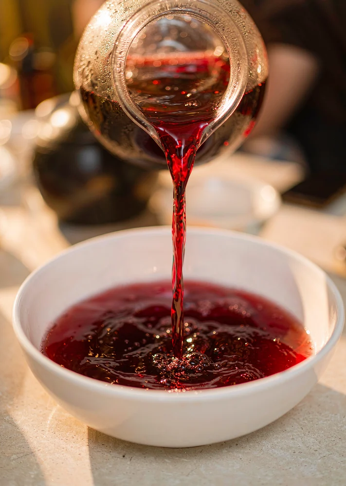 Deep-red punch being poured from a jug into a wide white ceramic bowl