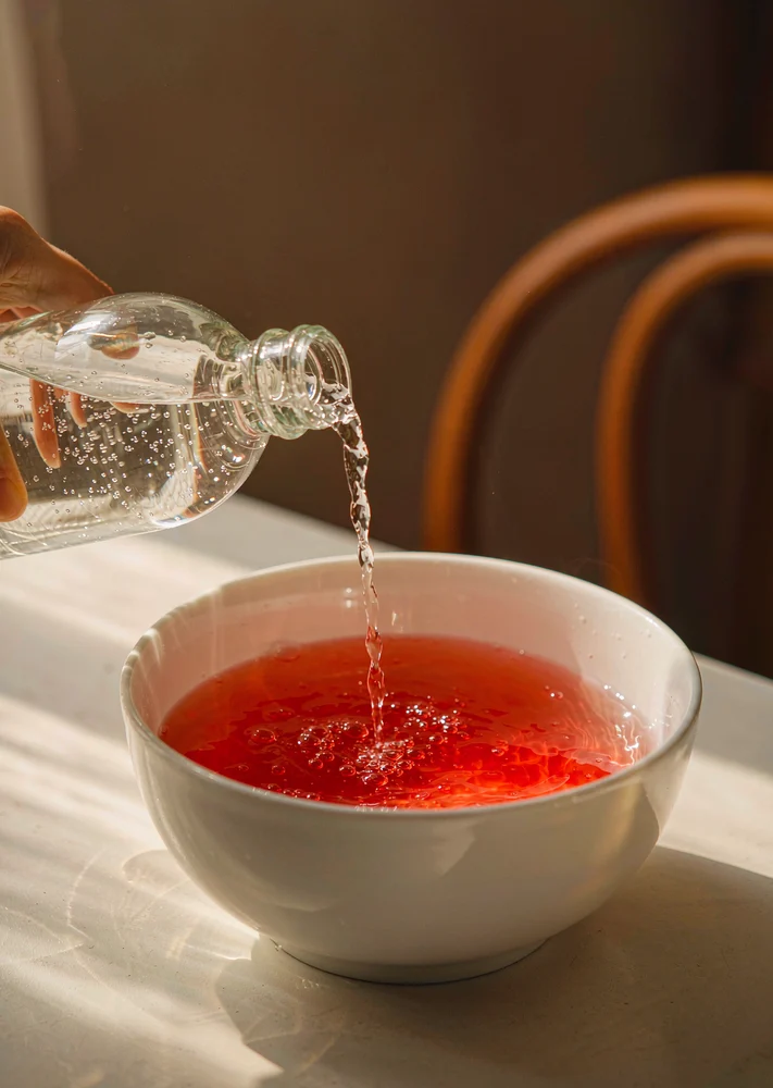 Sparkling water poured slowly down the inside of a white ceramic bowl of red punch