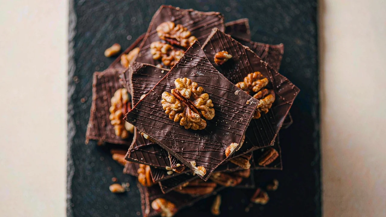 Pecan chocolate bark broken into pieces on a dark slate board, overhead view