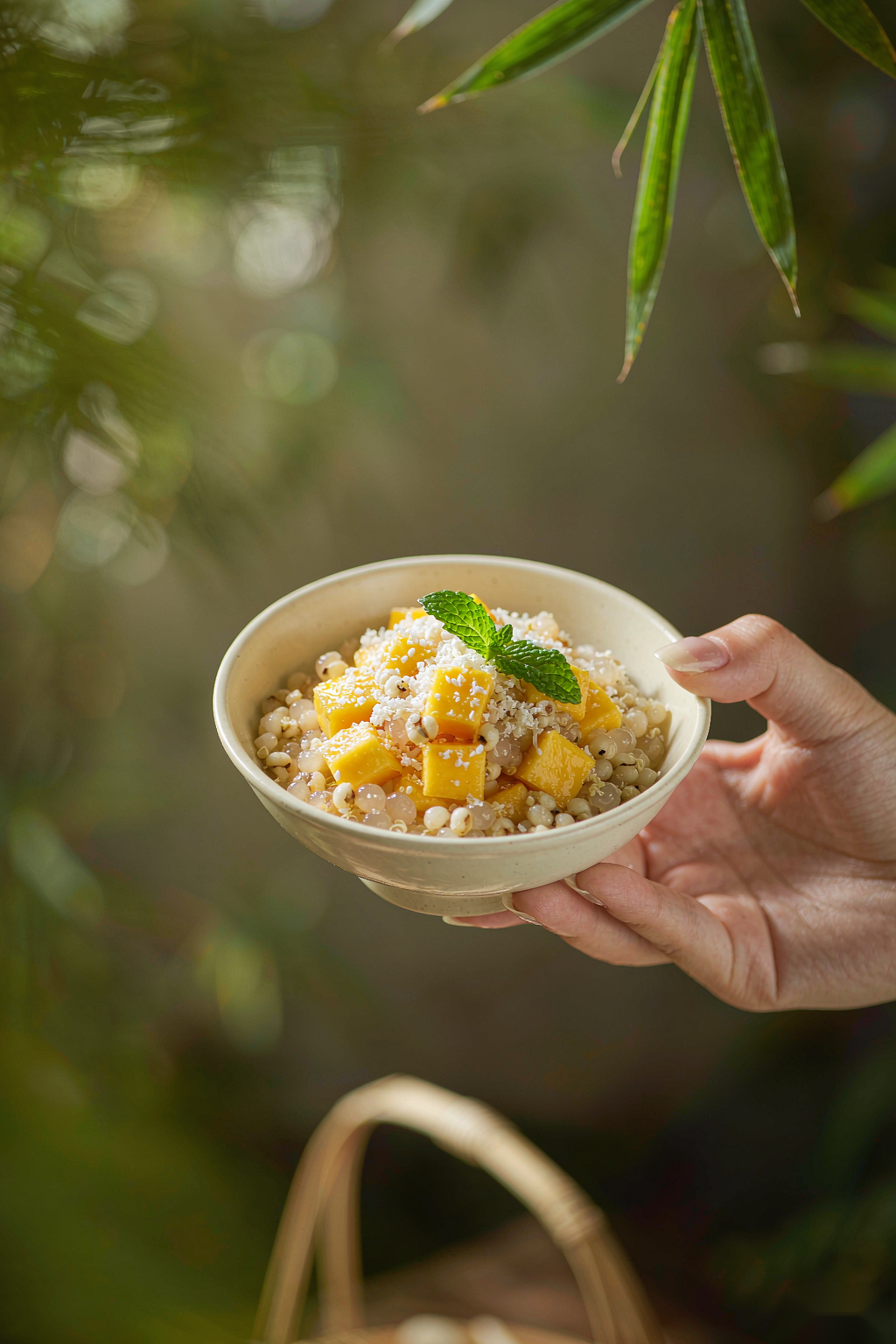 Lifestyle shot holding coconut mango quinoa bowl against tropical garden background with bamboo leaves