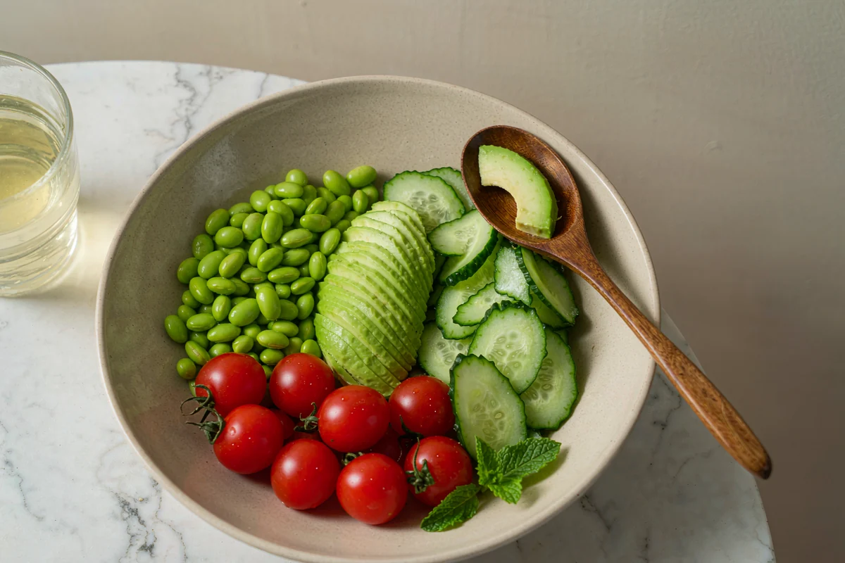 No-Cook Edamame and Avocado Bowl being assembled in a matte ceramic bowl with a wooden spoon