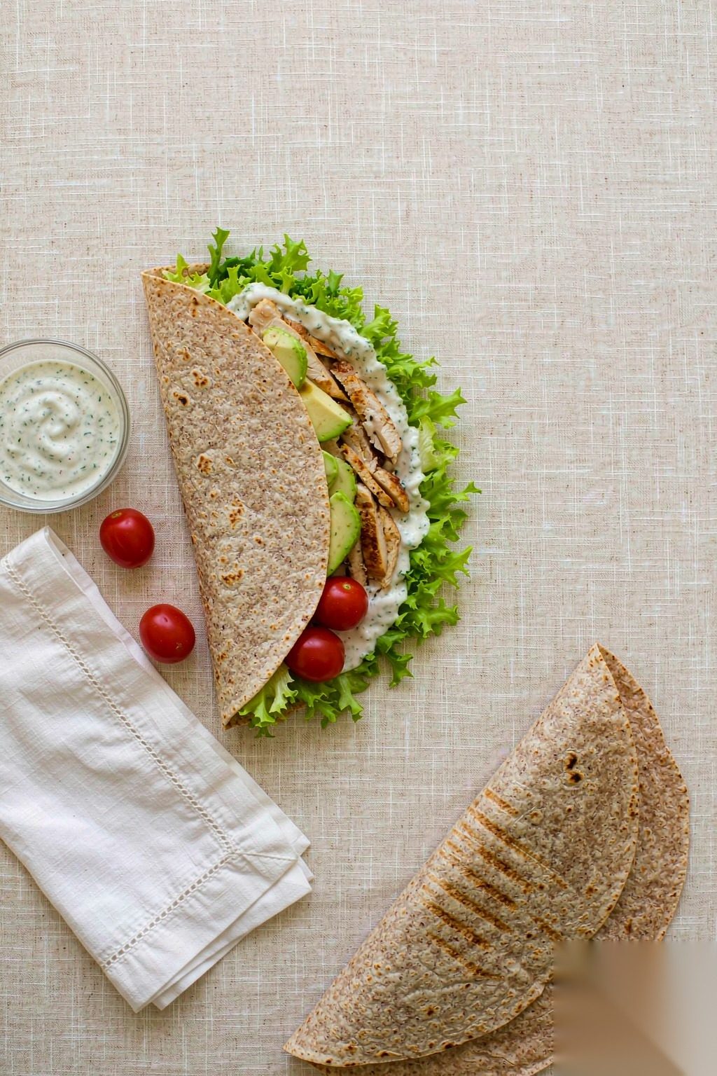 Grilled Chicken Power Wrap ingredients flat lay: whole wheat tortilla, grilled chicken strips, avocado, romaine, tomato and Greek yogurt sauce