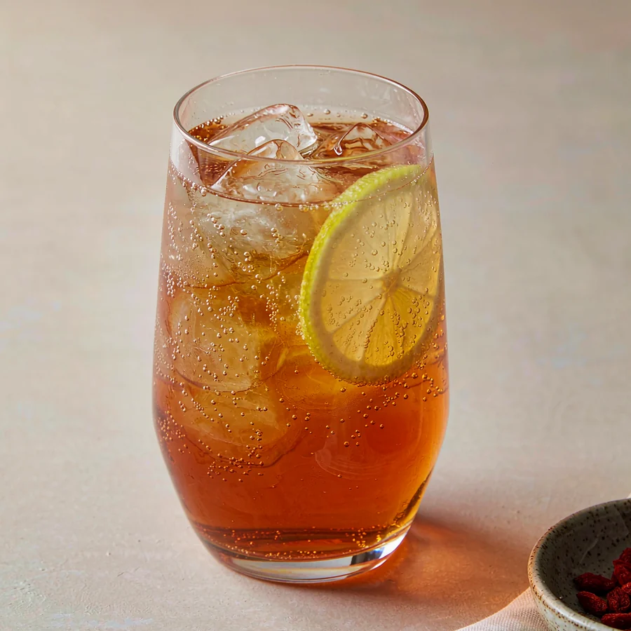 A clear glass of sparkling oolong kombucha with ice and lemon