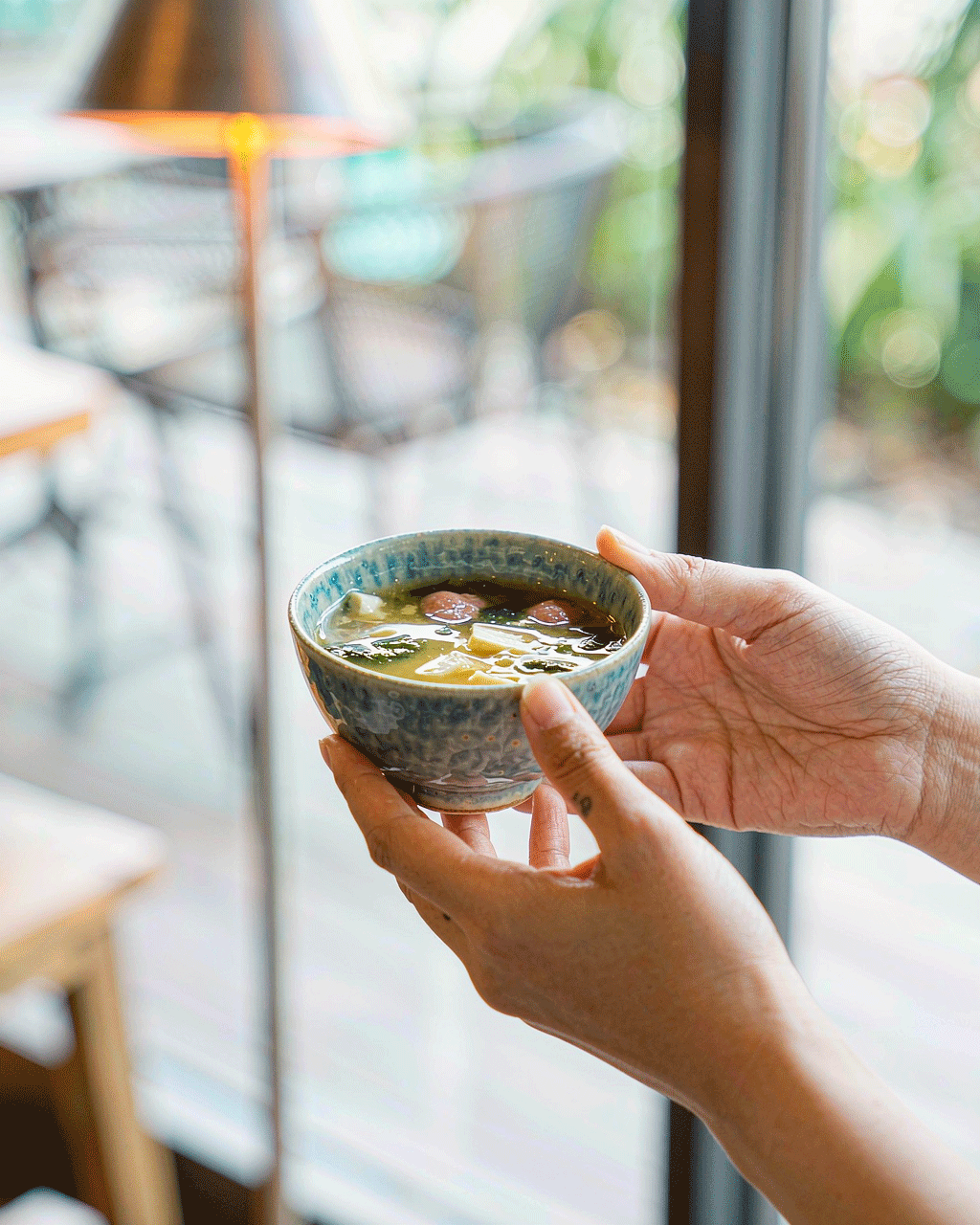 Lifestyle shot — hands holding a bowl of miso soup in a bright cafe