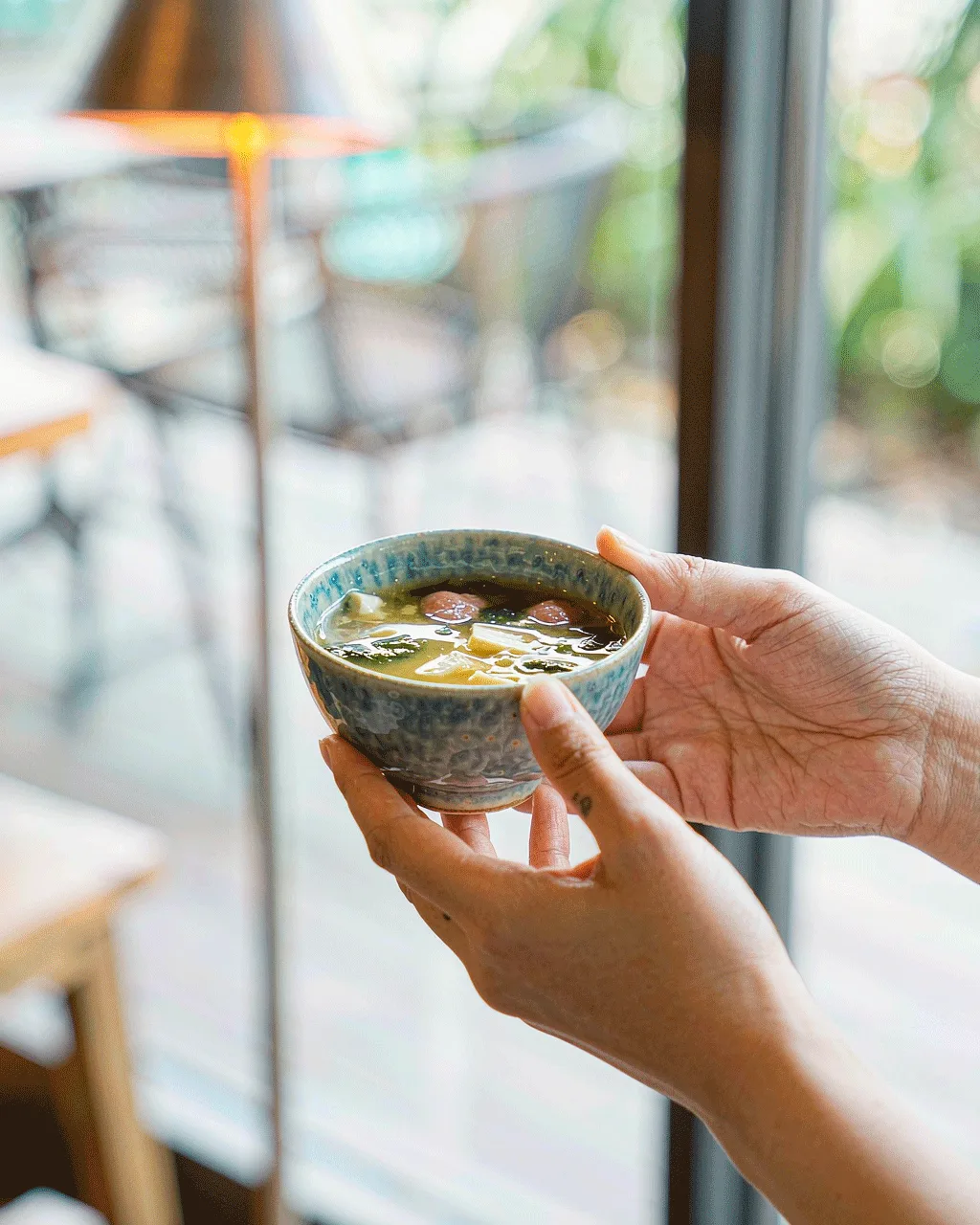 Lifestyle shot — hands holding a bowl of miso soup in a bright cafe