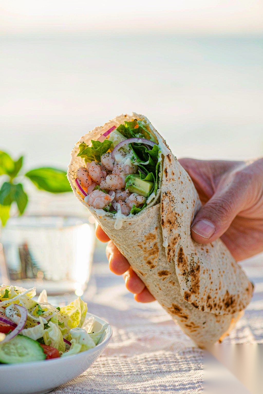 Shrimp Avocado Wrap held in hand at a beachside healthy lunch setting