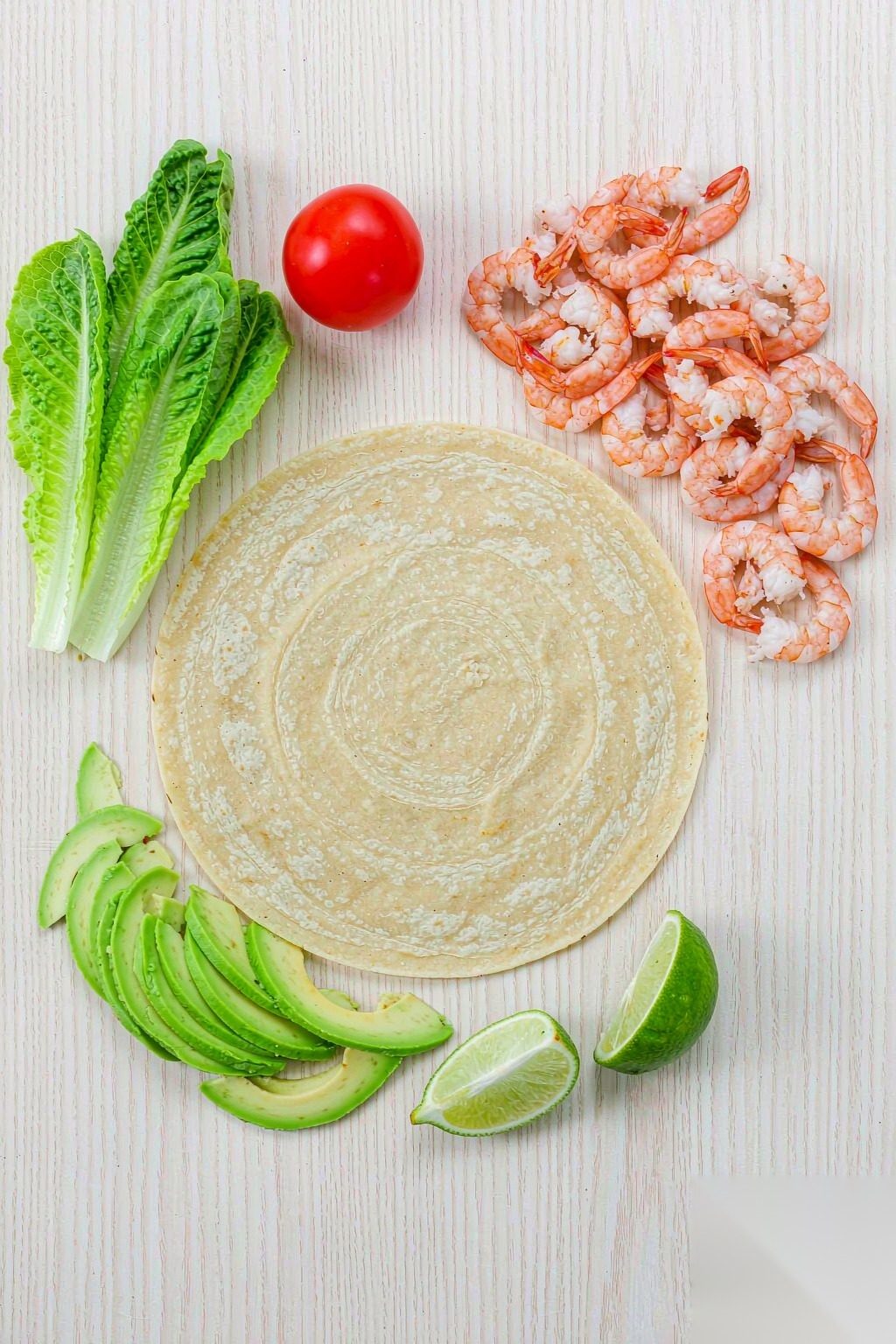 Shrimp Avocado Wrap ingredients flat lay: tortilla, cooked shrimp, avocado slices, romaine, cherry tomato and lime