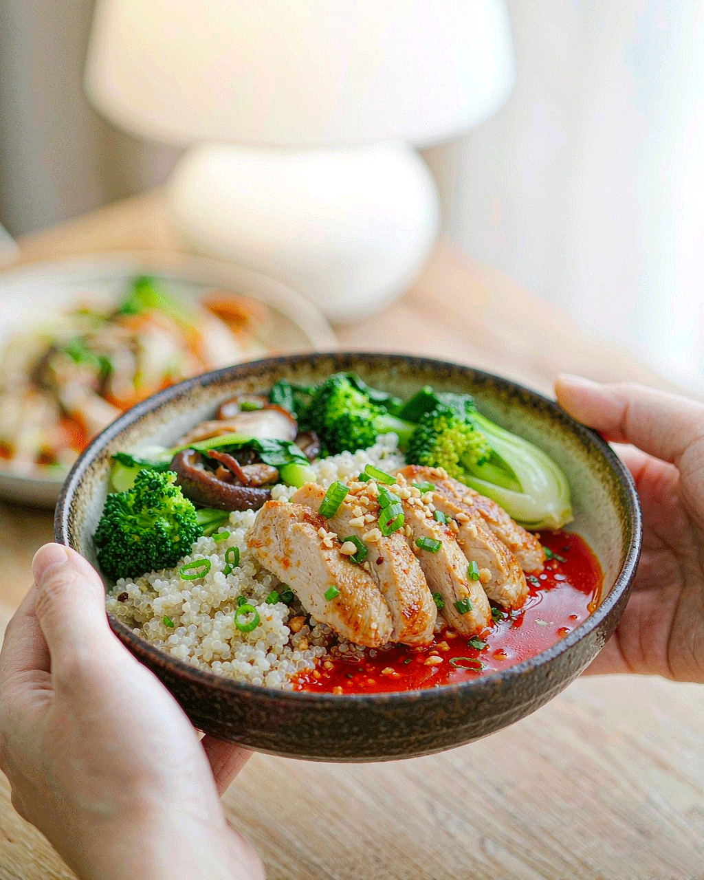 Lifestyle shot — hands holding the chicken quinoa bowl in a bright cafe