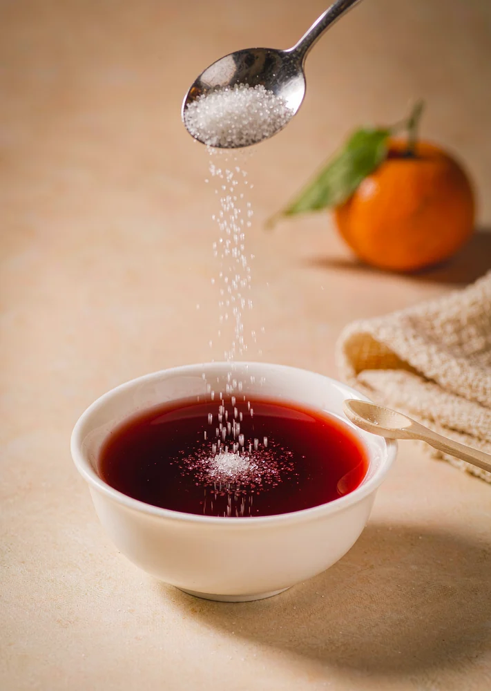 White ceramic bowl of red fruit punch with a spoon of erythritol sweetener on a light tabletop